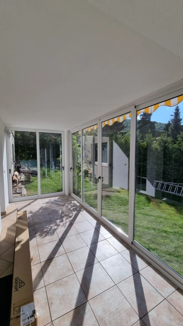 A glass-enclosed terrace with white frames and a view of the garden