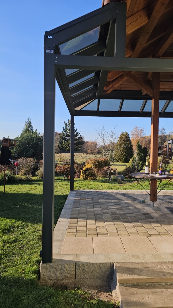 A close-up view of the aluminum structure and the glass roof of the pergola, offering a view of the garden.