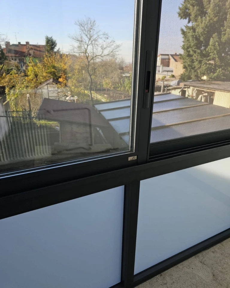 A close-up view of the sliding glass panels and frame of a sunroom overlooking the outdoors.