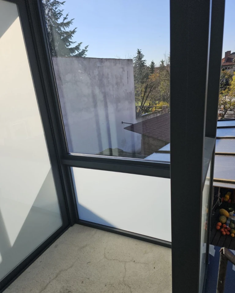 A close-up of the aluminum structure of the Robust conservatory, with a view of the surrounding buildings and trees in Brno.