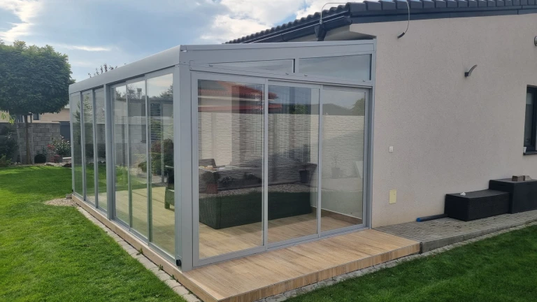 A modern, glass-enclosed sunroom with an aluminum frame attached to a single-family home