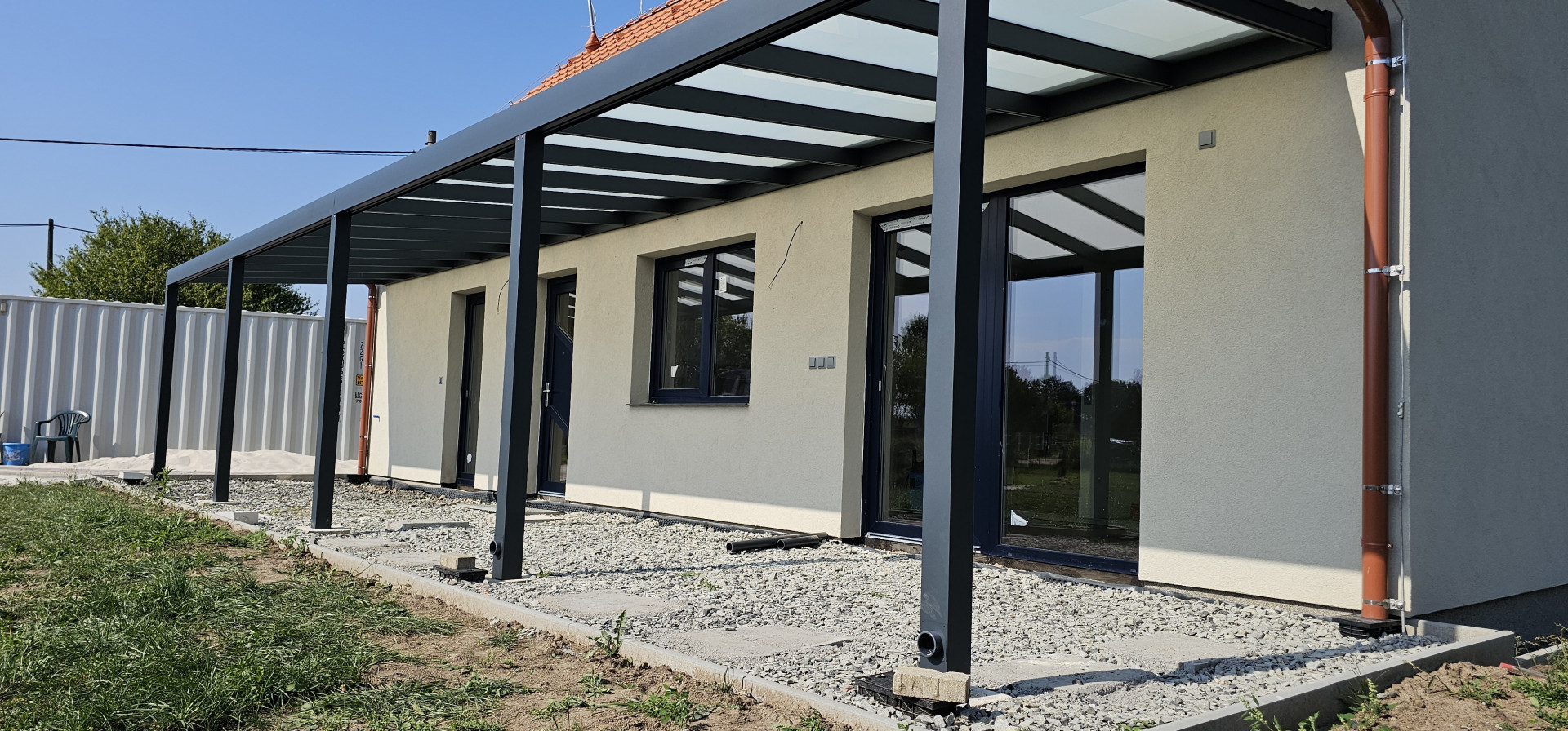 A modern aluminum pergola with a glass roof attached to the wall of a single-family home
