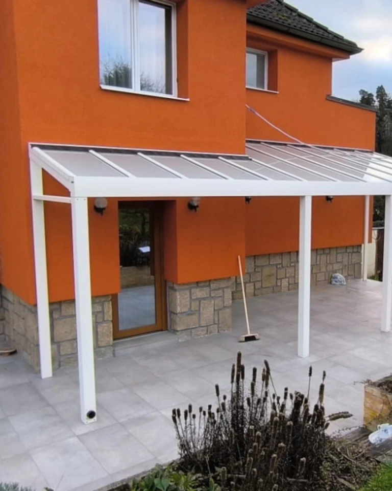 A white aluminum pergola with a glass roof attached to an orange house