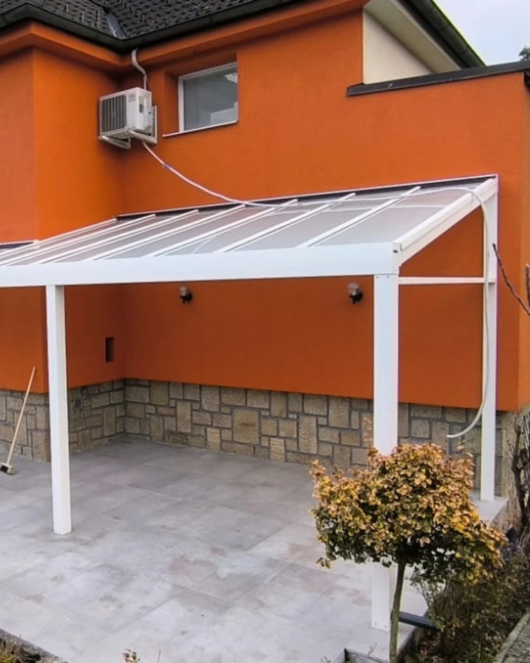 A white aluminum pergola with a glass roof attached to an orange house