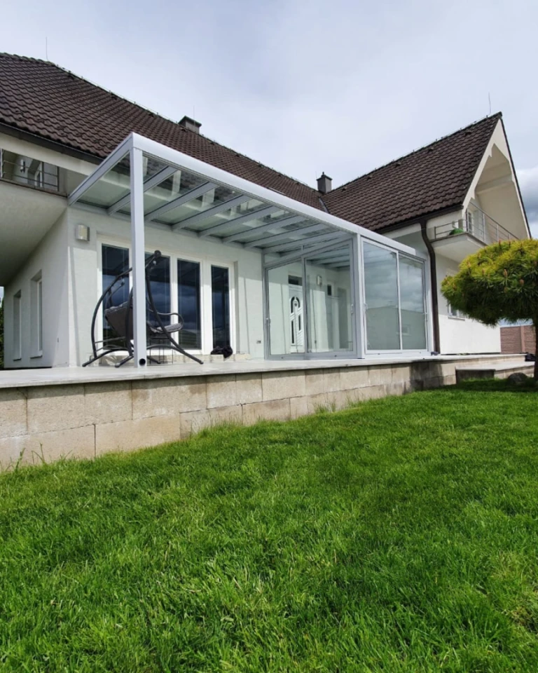 A modern aluminum sunroom with a glass roof and sliding doors on the terrace of a single-family home