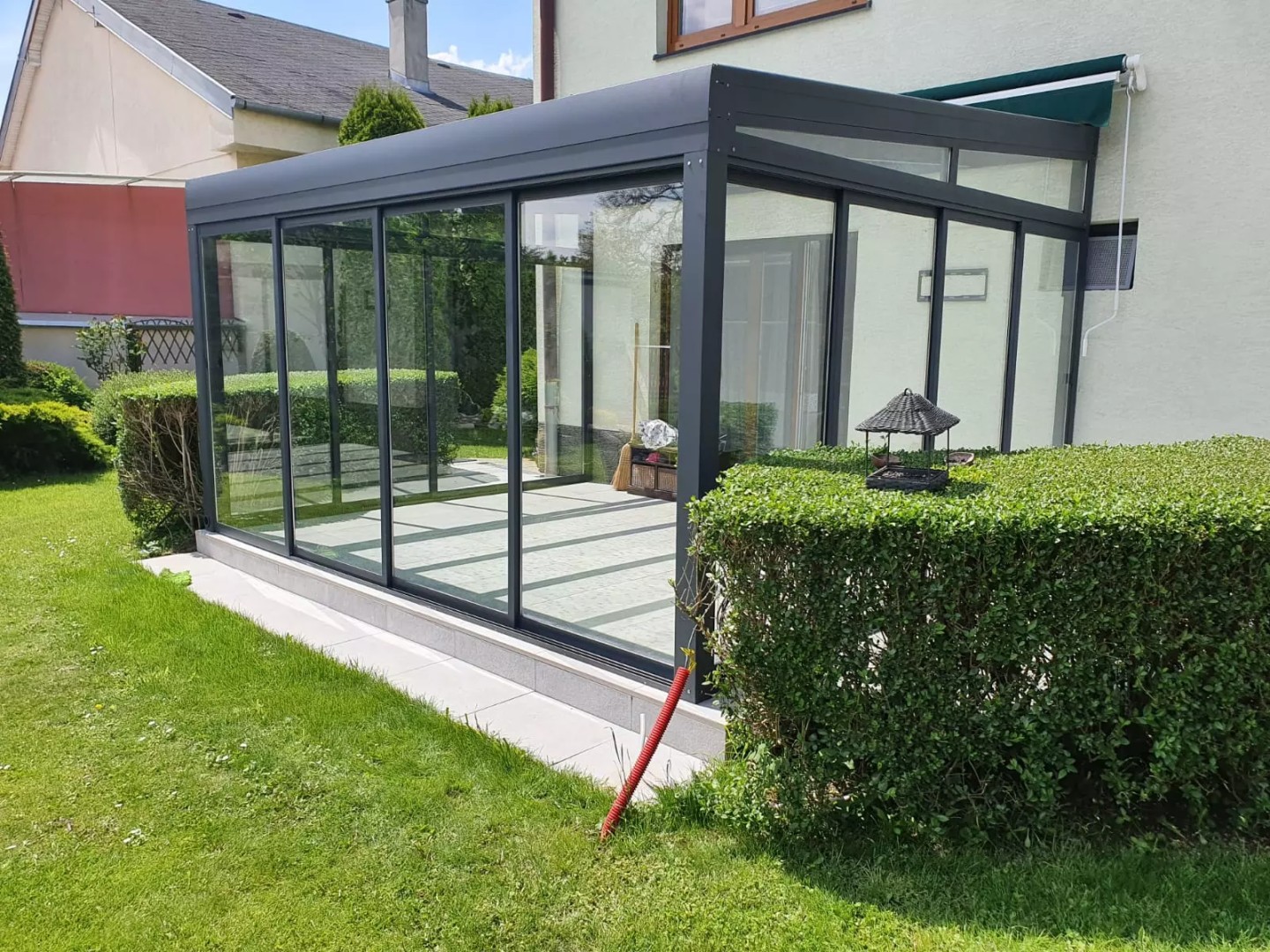 A modern glass-enclosed sunroom with an anthracite-colored aluminum frame, built next to a single-family home in the garden