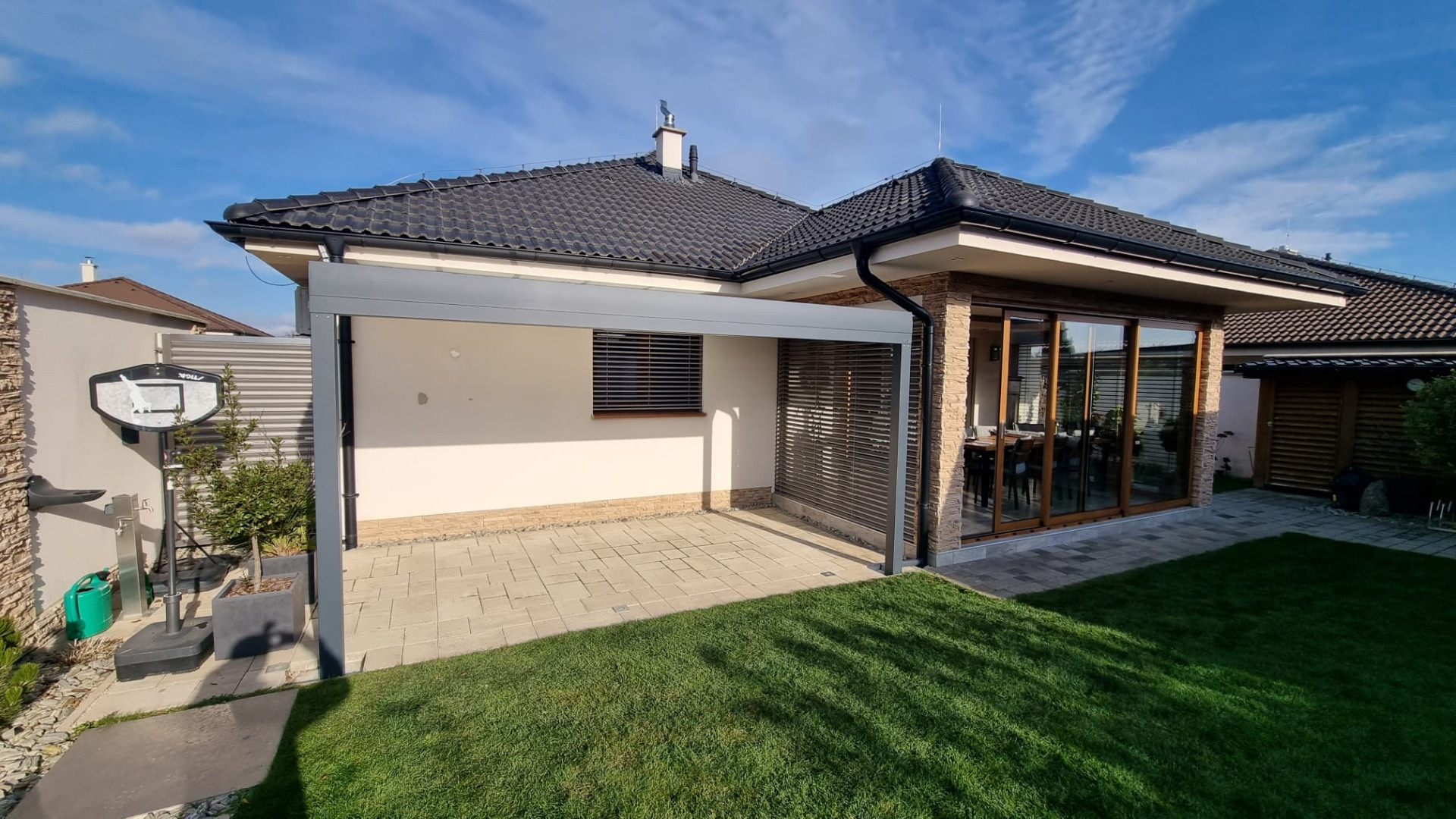A modern gray aluminum pergola next to the bungalow on a paved patio by the garden