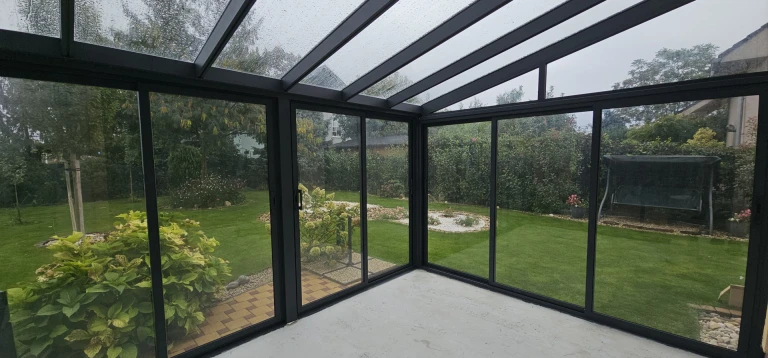 A view from inside the glass-enclosed sunroom overlooking the green courtyard and garden