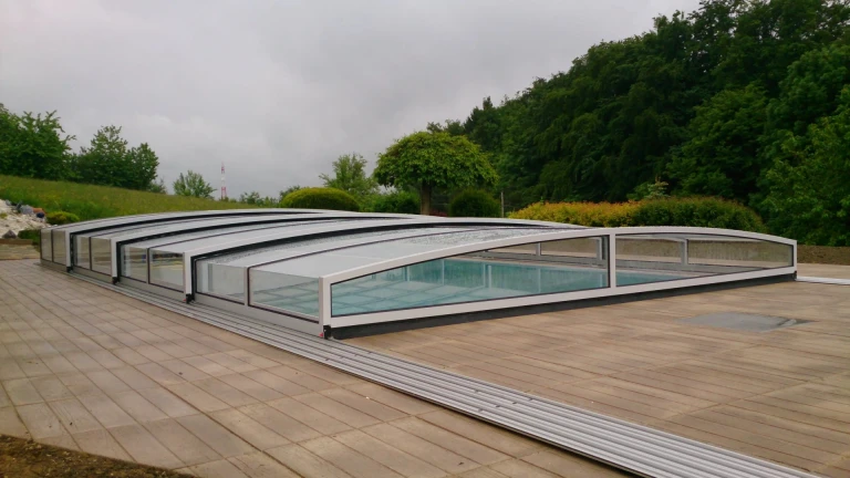 A low-profile STAR pool enclosure installed in a garden near the forest