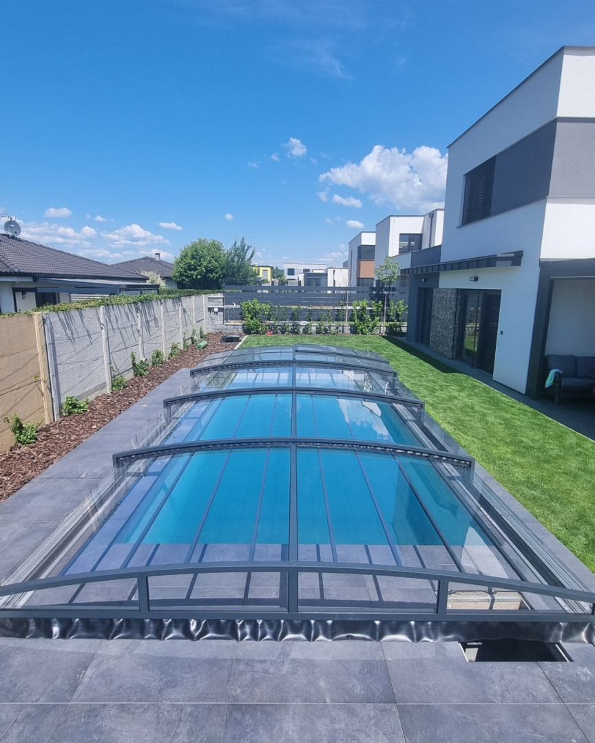 A modern, low-profile pool enclosure in anthracite color in a family backyard with a lawn