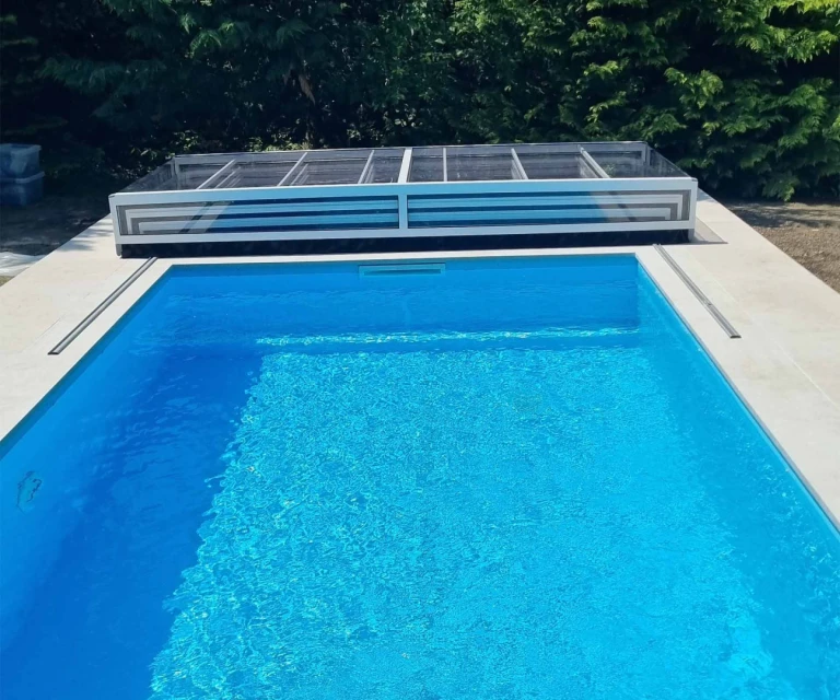 A view of the light blue pool with an open, low roof at the far end of the pool in the garden.