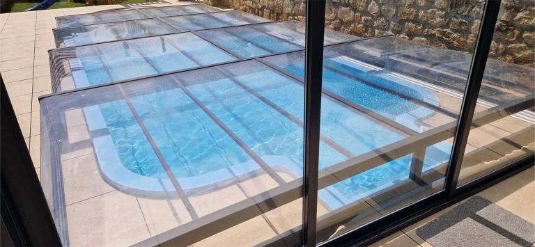 A view of the enclosed aluminum EXCLUSIVE pool enclosure with a transparent panel above the blue water