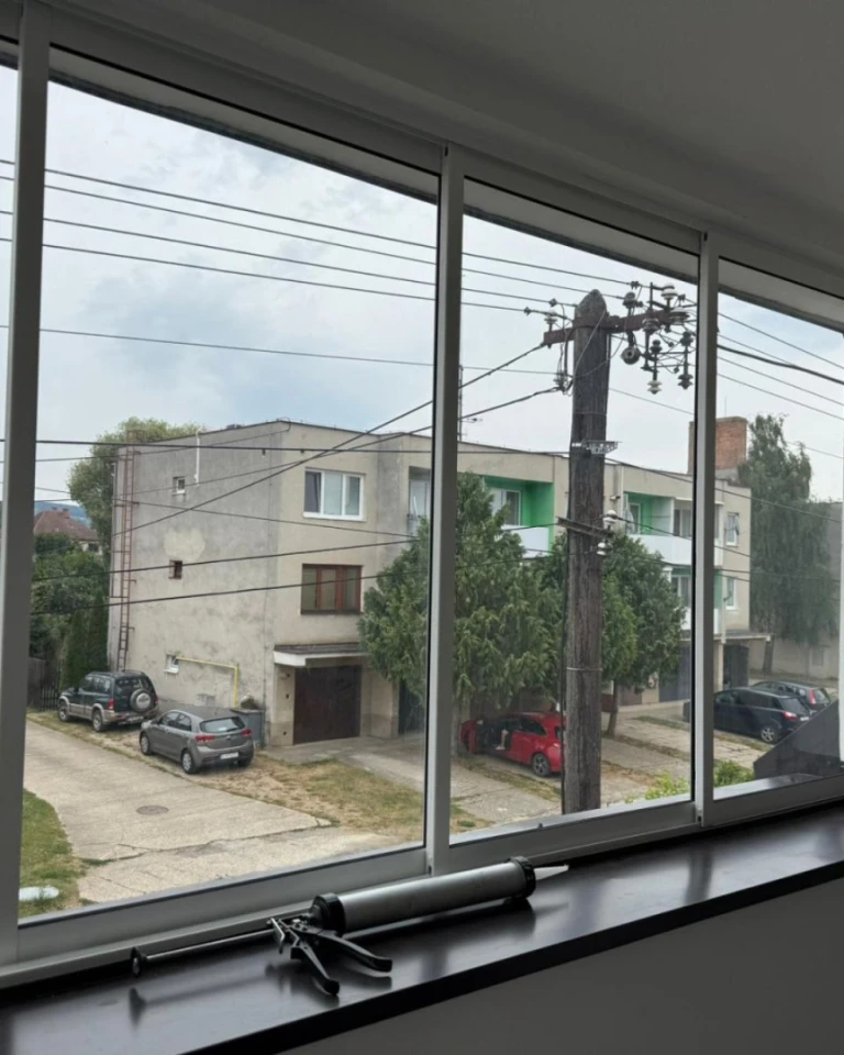 A view through the new windows onto the street with apartment buildings and cars; a glue gun lies on the windowsill