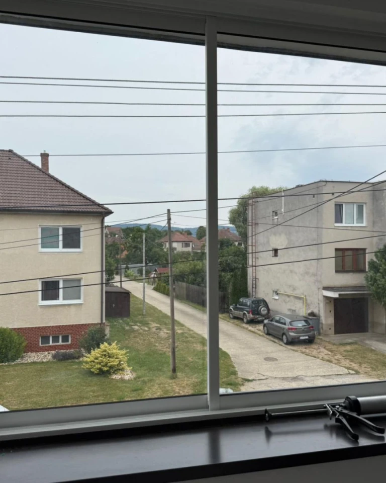 A view through the new windows of a street lined with single-family homes and cars in Skalica.