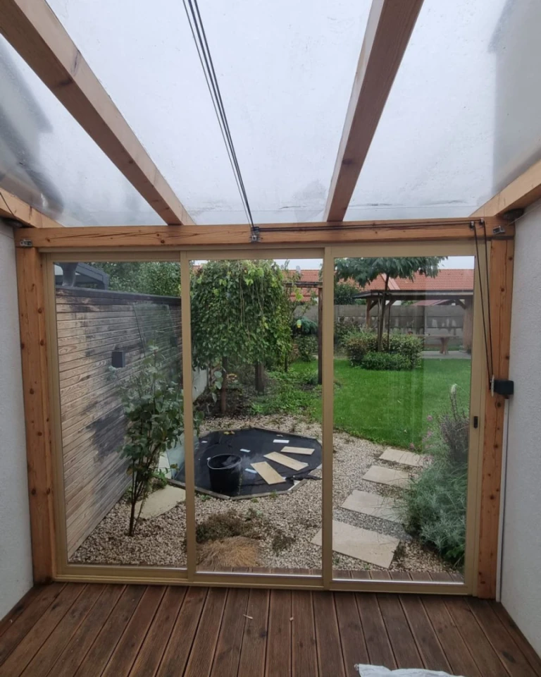 A view from inside the house of the glass-enclosed terrace with a wooden structure and a view of the garden