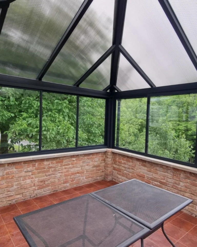 A modern glass-enclosed terrace with a brick wall and a view of the garden.