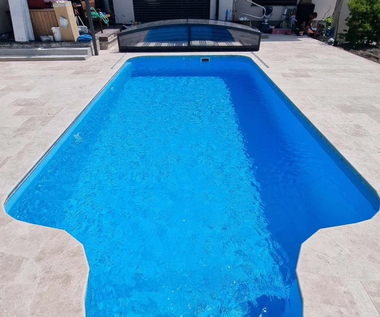 A view of an outdoor pool with blue water and a trackless pool cover in the background.