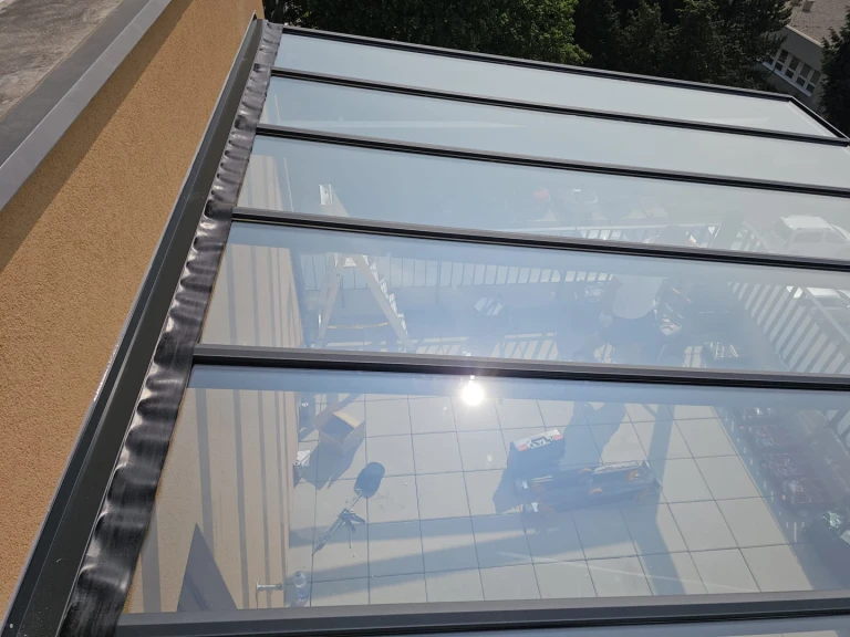 A close-up view of the glass roof of an aluminum pergola during installation on the patio.