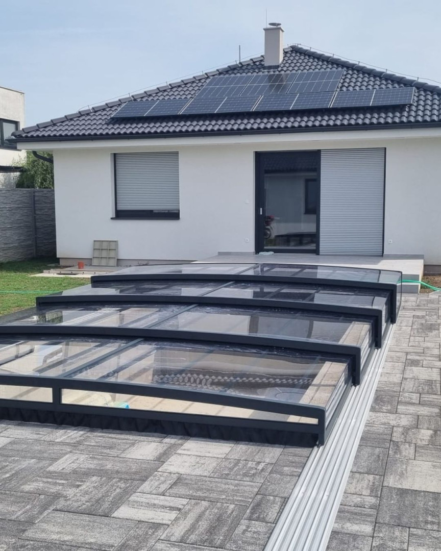 A modern, low-profile pool cover in anthracite in front of a single-family home with pavers and solar panels.