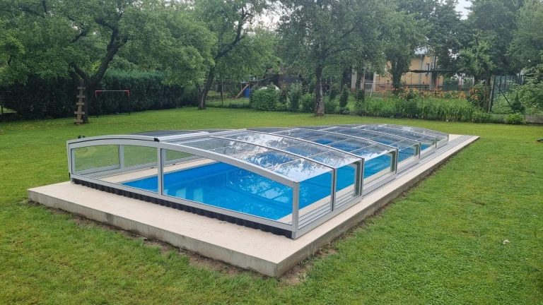 A modern, low-profile pool enclosure with transparent panels in the garden