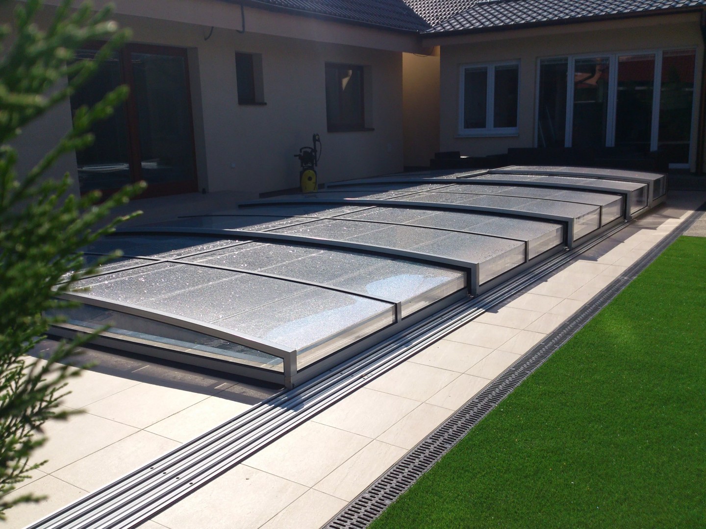 A low-profile STAR pool enclosure on the patio of a modern house with a lawn in Bratislava.