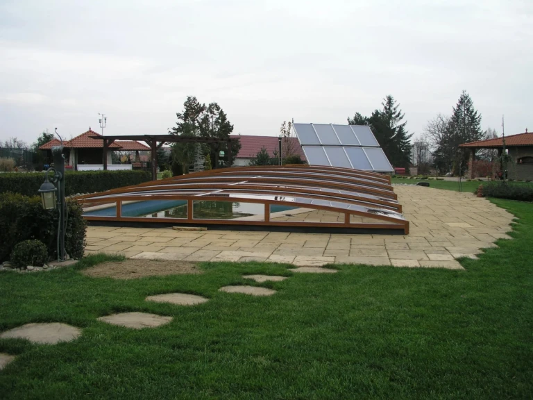 A low wooden pool enclosure in a garden with stone paving and solar panels in the background.