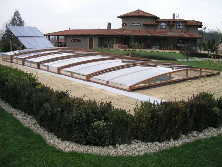 A low-profile pool enclosure with a wood-grain finish in the garden of a single-family home.