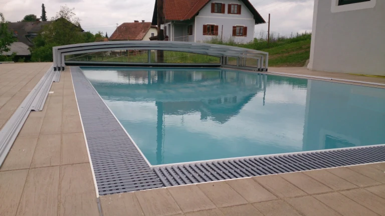 A modern swimming pool with an offset, low-sloped roof and stone paving in the garden of a single-family home.