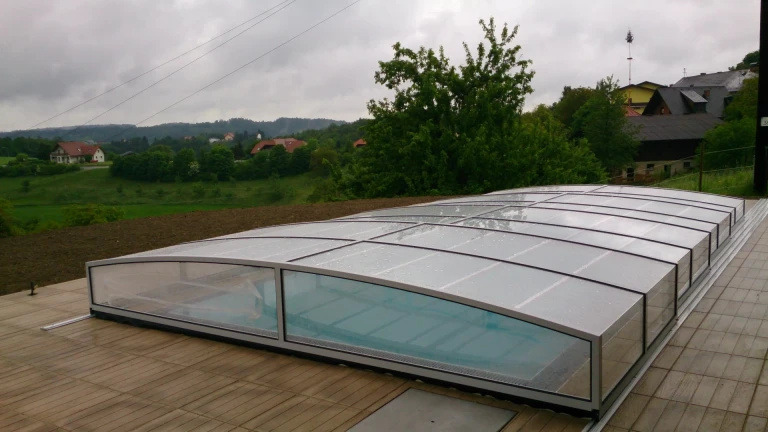 A modern, low-profile STAR pool enclosure on the terrace of a single-family home in a natural setting