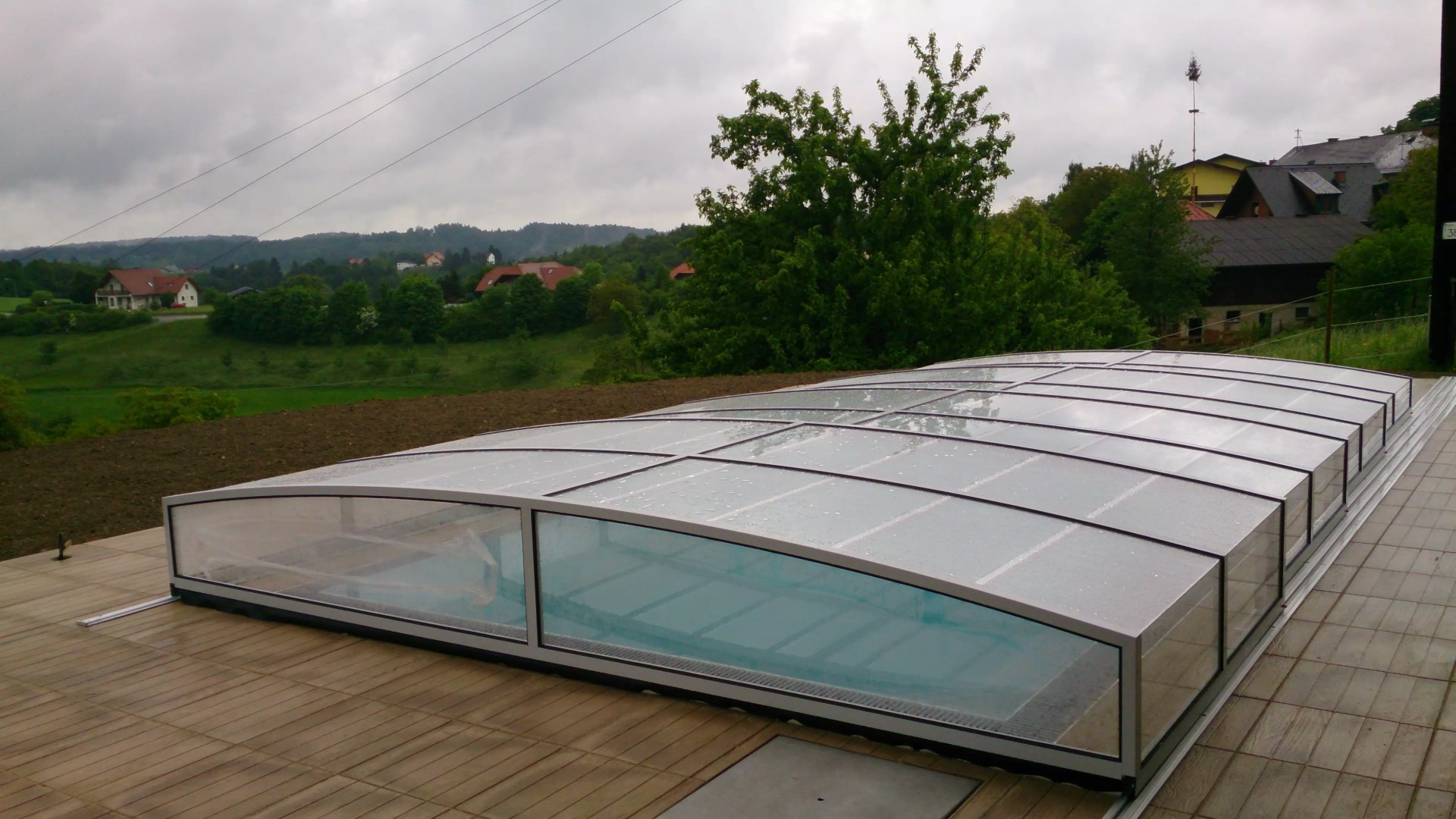 A modern, low-profile STAR pool enclosure on a terrace overlooking the hilly landscape and houses.