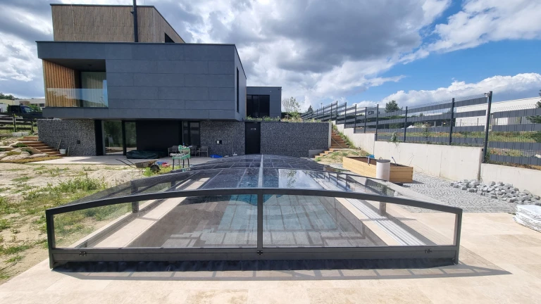 A modern single-family home with a low, anthracite-colored roof covering the pool on the terrace.