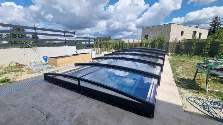 A modern, low-profile pool enclosure with a black frame and clear panels in the backyard of a single-family home.