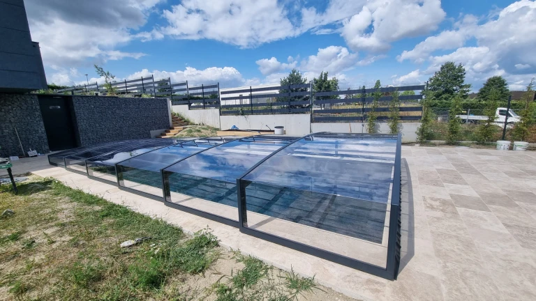 A modern, low-profile pool enclosure with a dark frame and clear glass on the terrace of a single-family home.
