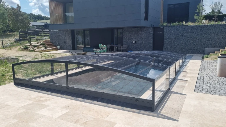 A modern, low-profile, dark-colored pool canopy in front of a modern, stone-clad house.