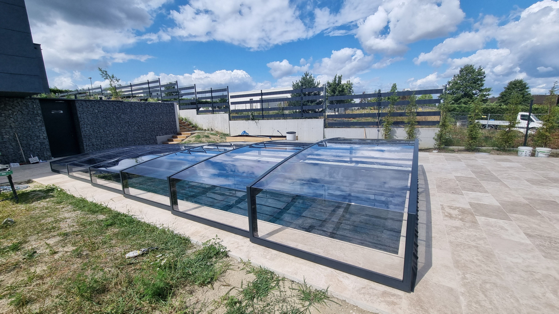 A modern, low-profile pool enclosure with dark frames and clear panels on the patio of a single-family home