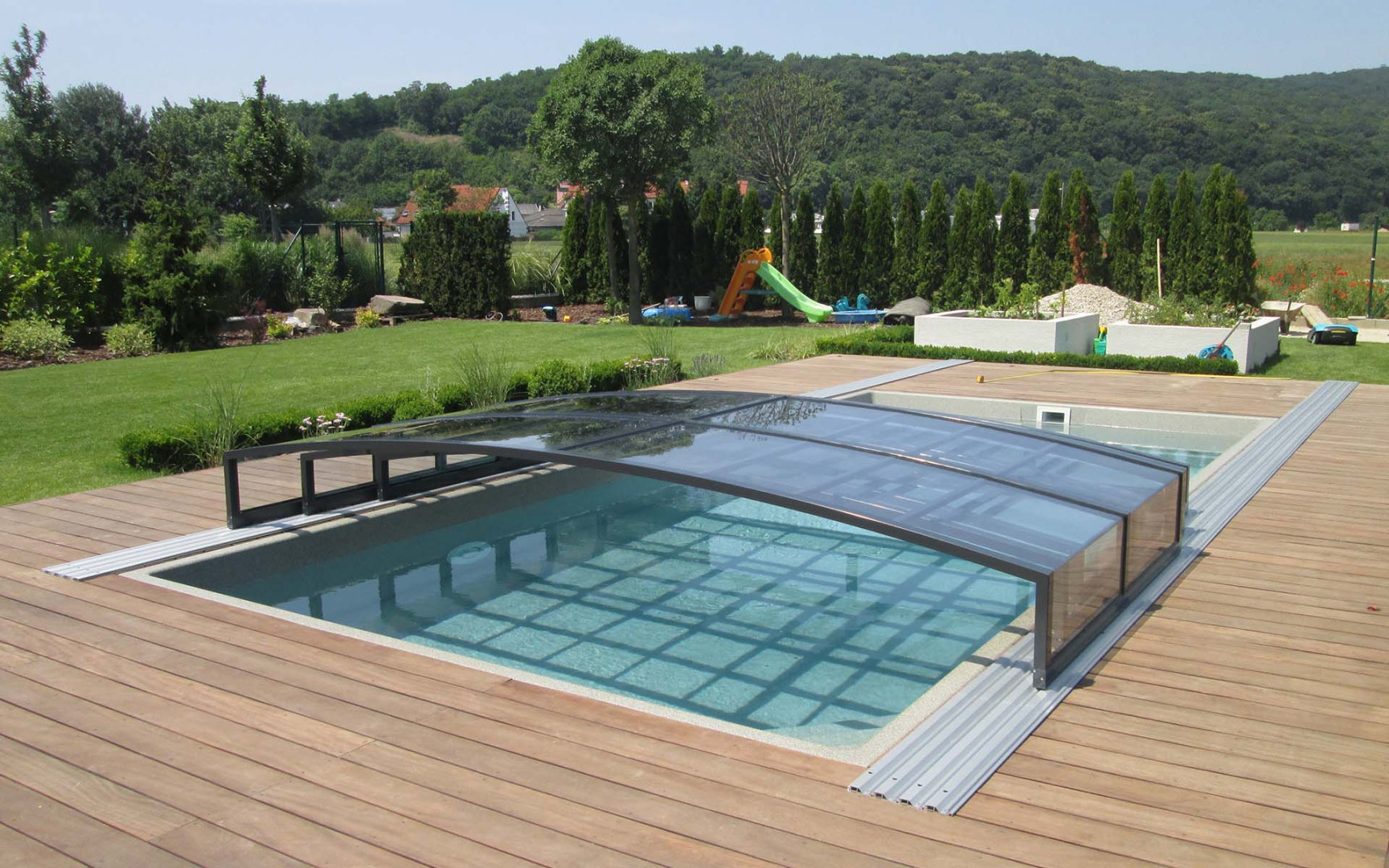 A modern swimming pool with an elegant low roof and a wooden deck in the garden.