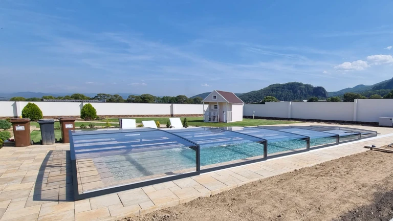 A modern, low-profile aluminum pool enclosure with an anthracite frame and clear panels in the garden of a single-family home
