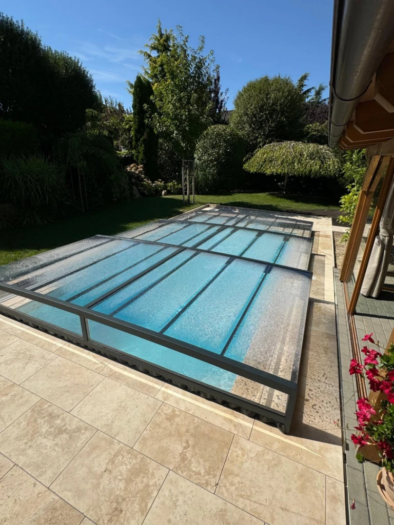 A modern, low-profile pool cover with a dark frame and clear panels in the garden