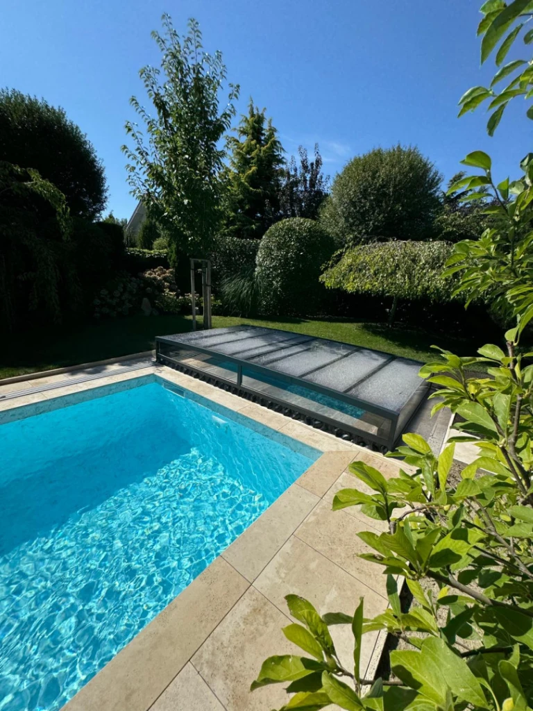 A modern, low-profile pool enclosure in the garden with clear blue water.