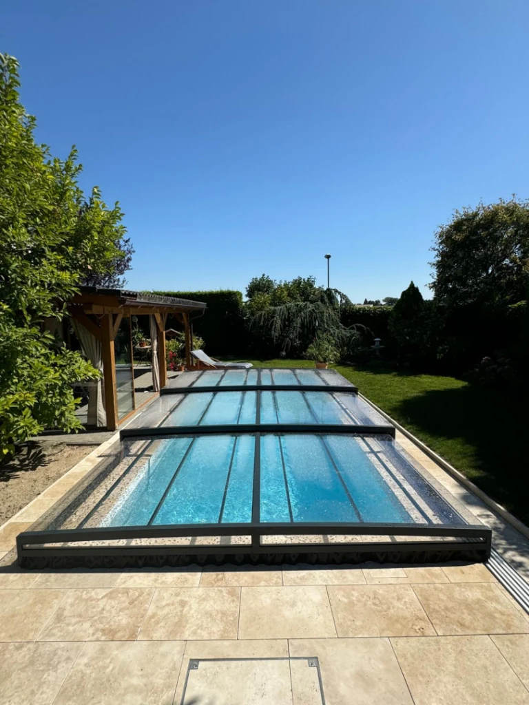 A modern, low-profile pool enclosure in a garden with a patio and a gazebo