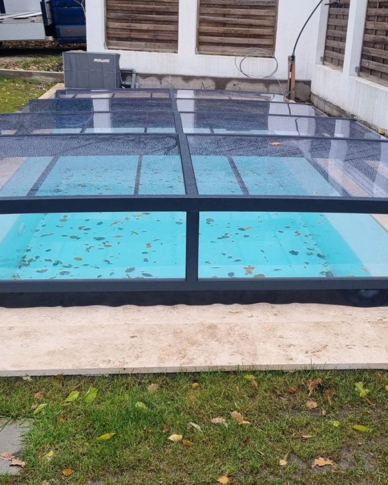 A modern anthracite-colored pool enclosure with a clear panel on the garden patio