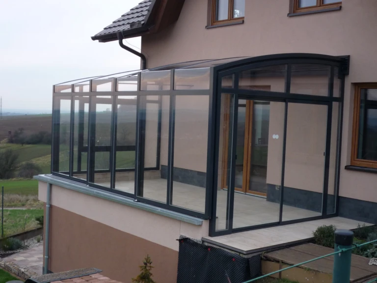 A modern sliding-glass conservatory on the terrace of a single-family home with a view of the countryside.