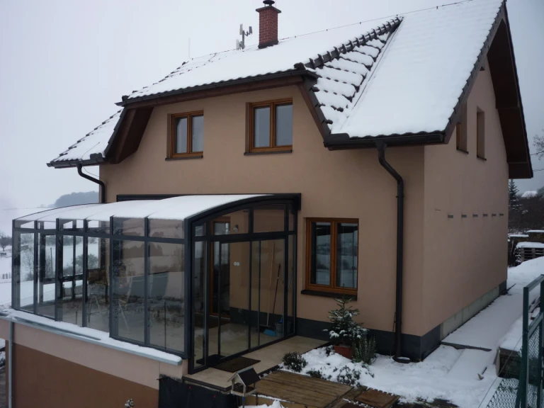 A glass-enclosed sliding sunroom on the terrace of a single-family home, covered in snow