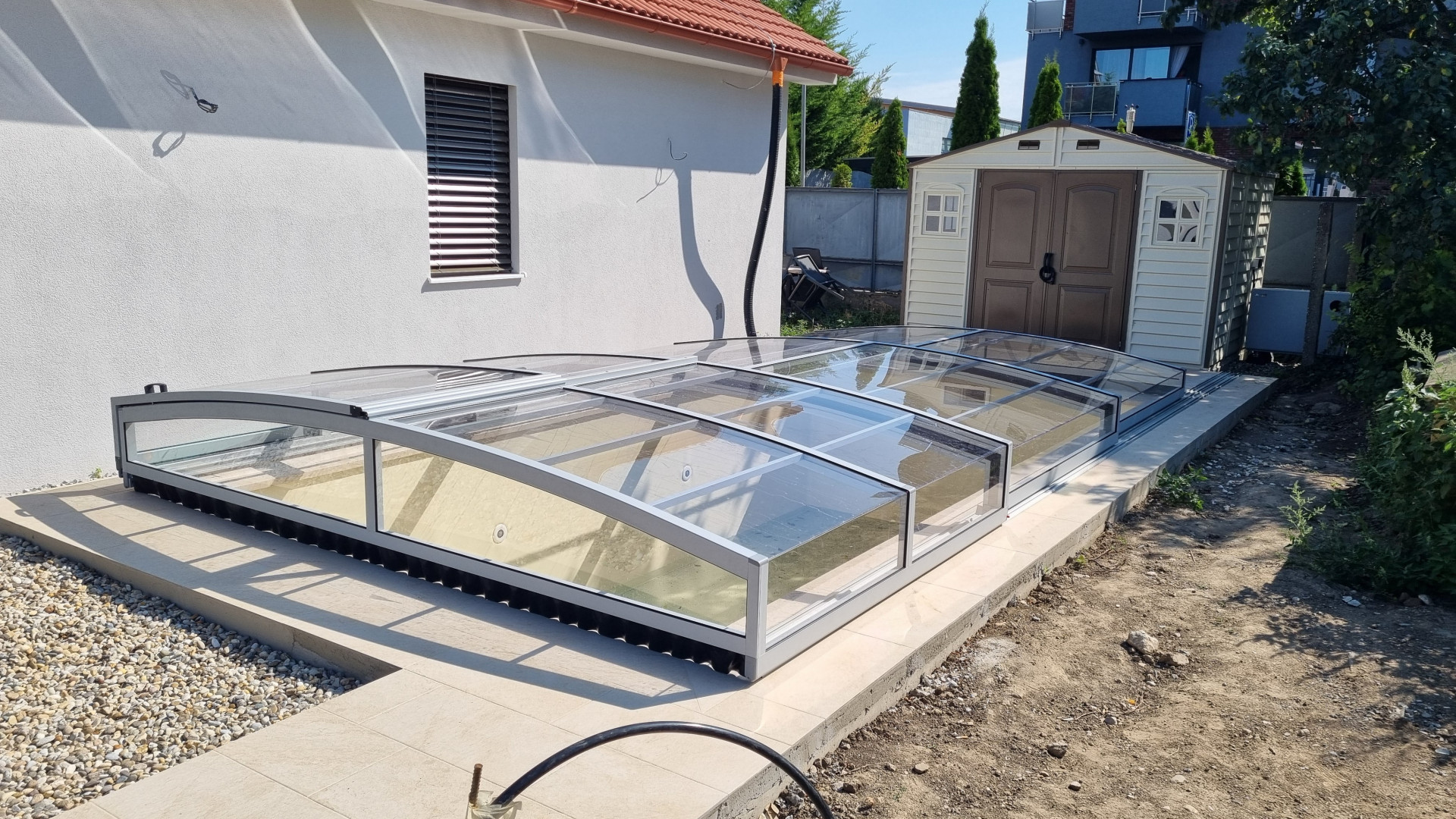 A low-profile segmented pool enclosure with a silver frame and clear polycarbonate at a single-family home in Senec.