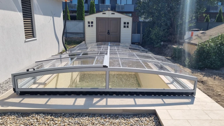 A modern, low-profile pool enclosure with a transparent panel in the garden of a single-family home