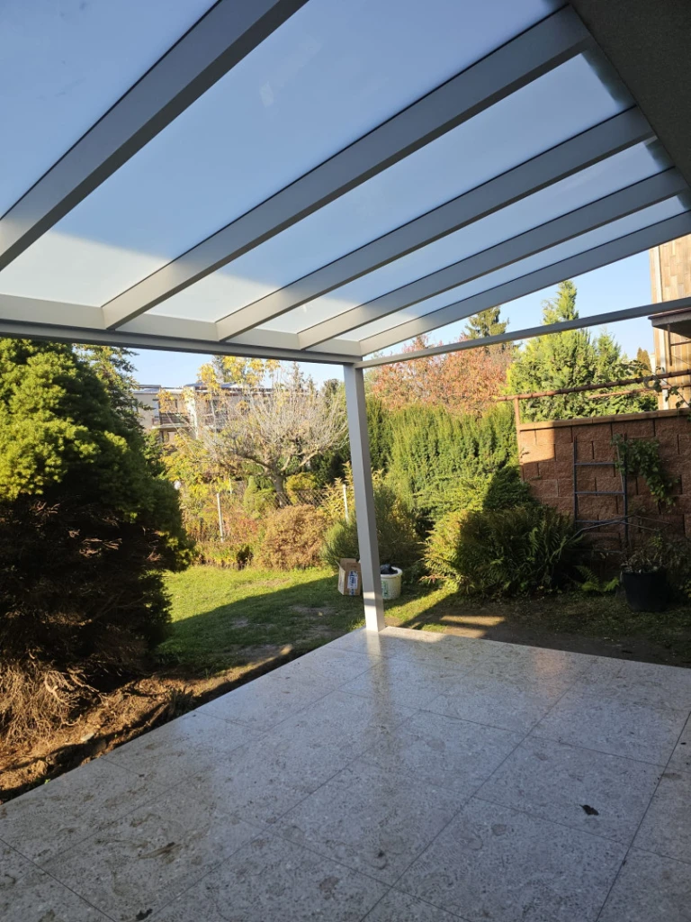 A modern aluminum pergola with a glass roof over the patio overlooking the garden