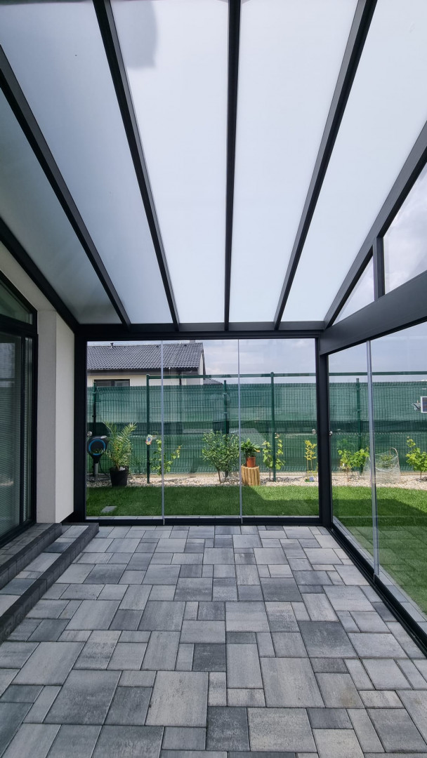 An interior view of a glass-enclosed sunroom with tiled flooring and a view of the courtyard