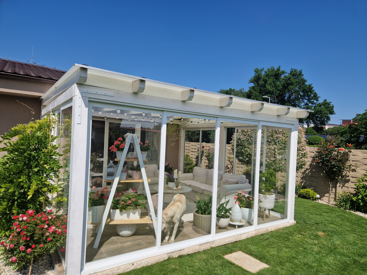 A modern white glass-enclosed sunroom with floral decorations and furniture in the garden of a single-family home