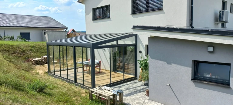A modern, glass-enclosed sunroom with a dark frame attached to a single-family home
