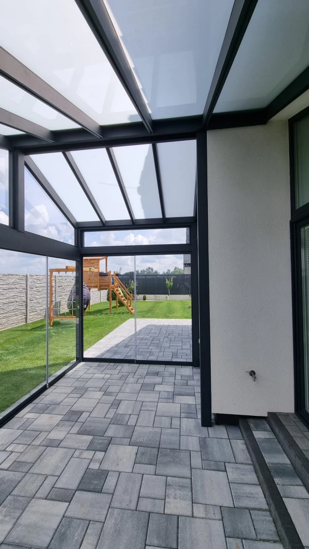 A glass-enclosed sunroom with an aluminum frame and a view of the backyard with a playground